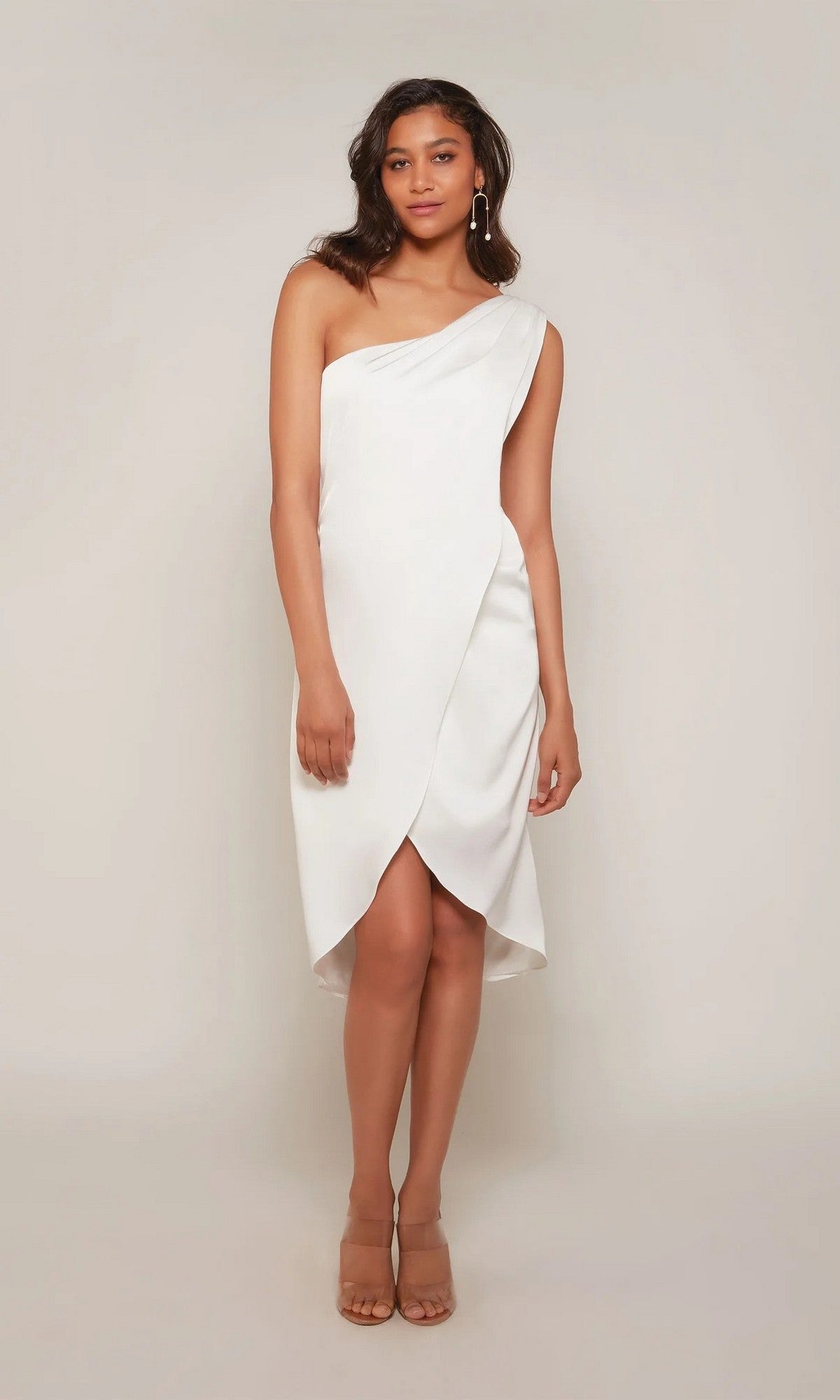 A woman models the Alyce 70038 knee-length party dress in Diamond White, featuring a one-shoulder design and nude heels, against a plain light background.